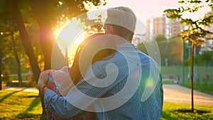 Shooting from the back, lovely caucasian couple holding each other, standing and looking ahead in sunlights, park