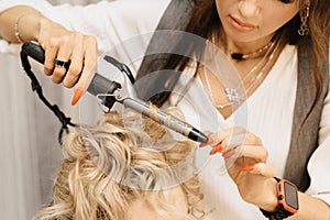 Shooting in a beauty salon. A hair stylist makes a hairstyle for a young dark-haired girl with the help of a hair styler