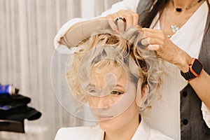 Shooting in a beauty salon. A hair stylist makes a hairstyle for a young dark-haired girl with the help of a hair styler