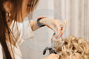 Shooting in a beauty salon. A hair stylist makes a hairstyle for a young dark-haired girl with the help of a hair styler