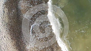 Shooting from the drone. Top view of a small wave with white foam, runs ashore. No sound.