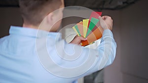 Shooting over shoulder of blurred Caucasian man choosing color planning wall painting in new apartment. Young flat owner