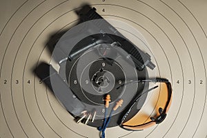 A shooting target with bullet holes in the center, a G19 gen5 pistol, goggles, earplugs, and a magazine with ammo