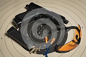 A shooting target with bullet holes in the center, a G19 pistol, goggles and earplugs, and a magazine with cartridges