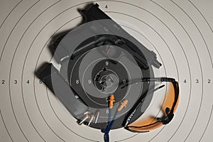 A shooting target with bullet holes in the center, a G19gen5 pistol, goggles and earplugs, and a magazine with cartridges