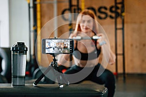 Shooting video by smartphone. Doing exercises. Beautiful strong woman is in the gym