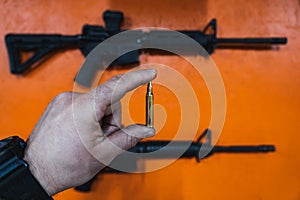 Shooting weapons in a shooting range. A 5.56x45mm cartridge in a man's hand and an m4a1 rifle on an orange wall