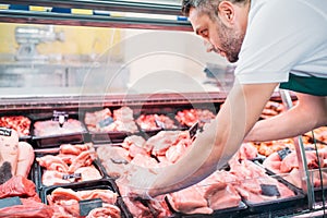 shop assistant in apron assorting fresh raw meat