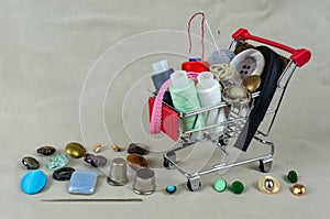 A shop basket with threads, sewing accessories and buttons. The background is made of gray-beige fabric