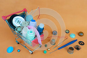 A shop cart with threads, sewing accessories and buttons. The background is made of light orange fabric