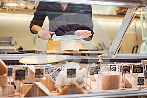 Shop clerk woman sorting cheese in the supermarket display