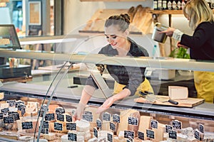 Shop clerk woman sorting cheese in the supermarket display