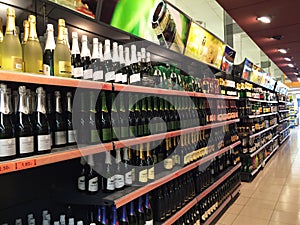 Shop shelves full with bottles of vine of different types stand in rows. Variety of alcoholic drinks