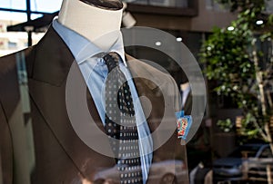 Shop window of mens tailor shop showing a mannequin in a brown tailored suit and blue tie