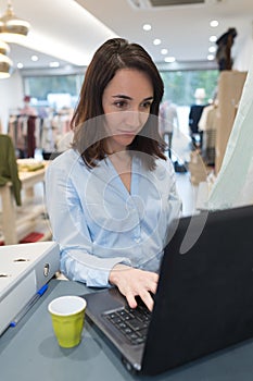 Shop worker using laptop by till