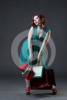 Shopaholic concept, young beautiful red-haired caucasian woman in aquamarine dress posing in studio on gray background, profession