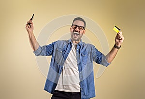 Shopaholic man with credit card and mobile phone screaming excitedly after winning rewards for online shopping. Young male