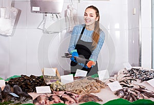 shopgirl with apron offering fresh fish in shop