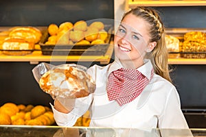 Shopkeeper in bakery presenting loaf of bread to client