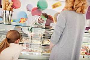 Shopkeeper in confectionery serves girl with ice cream photo