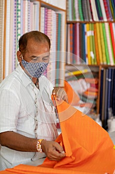Shopkeeper in medical mask measuring cloth using scale or ruler - concept of back to business, business reopen after