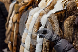 shopper with gloves examining a rack of fur coats