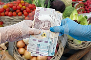 Shopper in gloves with hryvnia on the background of vegetables in the supermarket.  Close-up. Coronavirus protection concept