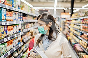 Shopper with mask safely shopping for groceries due to coronavirus pandemic in stocked grocery store.COVID-19 food buying.Non