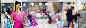 Shopper smiling with bags in blurry shopping centre