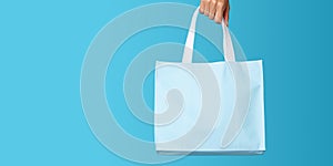 Shopping bag in woman's hand on blue background. Mockup design with blank space. Add text or logo. Generative Ai