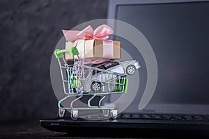 Shopping basket with car and gift box on laptop keyboard on dark background. Online shopping vehicles on the Internet
