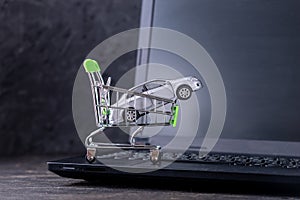 Shopping basket with car on laptop keyboard on dark background. Concept of online shopping vehicles on the Internet