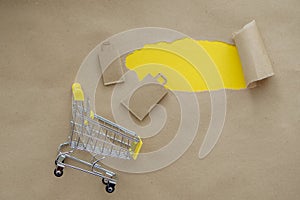 A shopping basket next to grocery bags and with a small hole in the paper with the sides torn off on a brown background