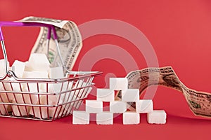 Shopping basket with sugar cubes and paper money bills on a red background. Selective focus. Copy space