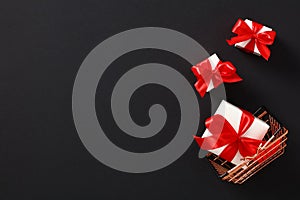 Shopping basket and white gift boxes with red ribbon bows on black background. Black Friday Sale banner template. Top view with