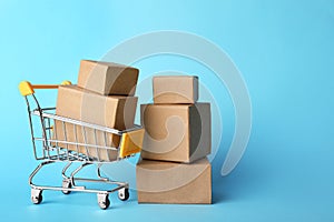 Shopping cart and boxes on blue background, space for text. Logistics and wholesale concept
