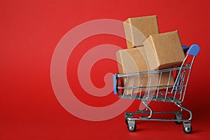 Shopping cart with boxes on red background. Logistics and wholesale concept photo