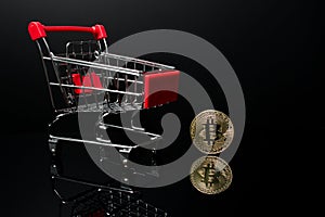Shopping cart with a crypto currency Bitcoin coin next to it with a black background.