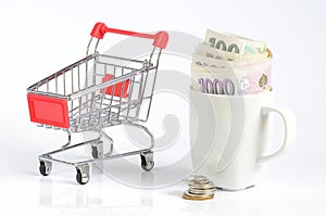 Shopping cart and czech coins and banknotes in white cup