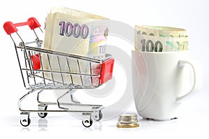 Shopping cart and czech coins and banknotes in white cup