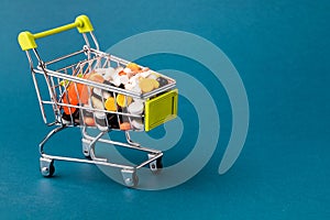 Shopping cart filled with pills. Blue background. Concept: full set of medicines in the store. Copy space for text
