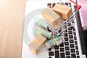 A shopping cart full of express parcels and a rolled Australian dollar bill next to it are placed on the laptop keyboard