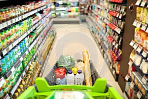 Shopping Cart Full Of Food Products Over Supermarket Aisle Background