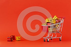 Shopping cart full of gifts on red background.  Close-up of shopping trolley on with some copy space. Consumer concept.