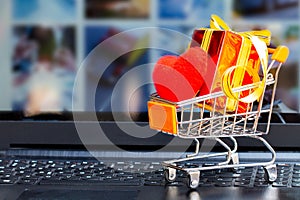 Shopping cart full of gold gift boxes and red sale sign through laptop monitor concept