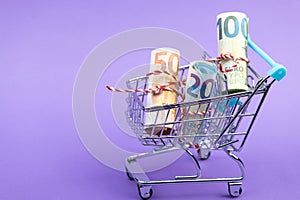 Shopping cart full of roll euro banknotes on purple