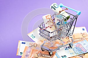 Shopping cart full of roll euro banknotes on purple