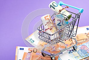 Shopping cart full of roll euro banknotes on purple