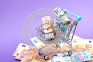 Shopping cart full of roll euro banknotes on purple