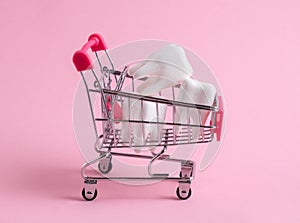 Shopping cart full of teeth on pink background. Investment in dental treatment, discounts at the dental clinic concept